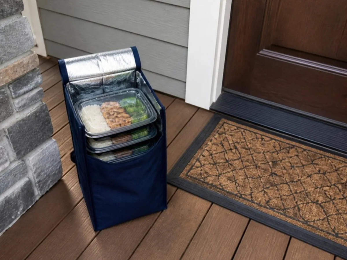 An insulated delivery bag of meals left on a front porch beside the door